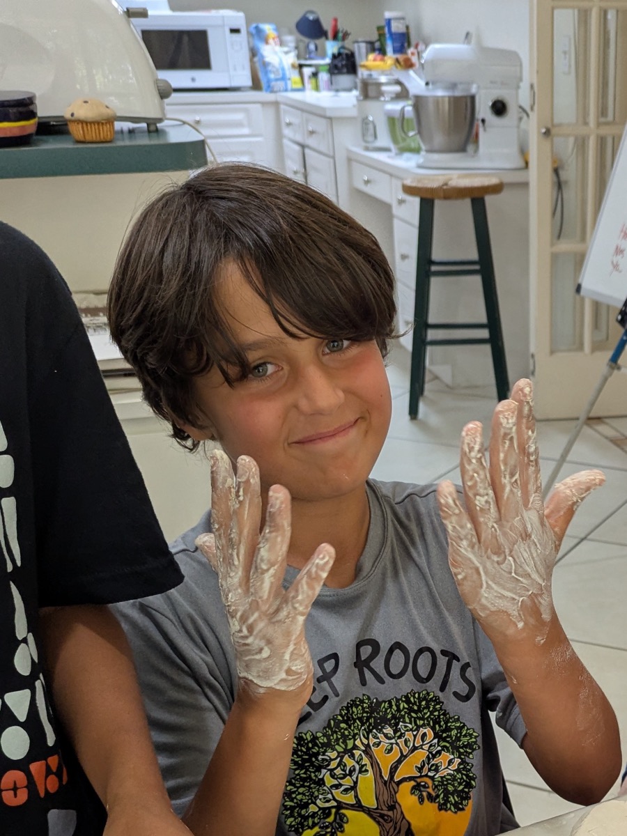 Student holding up clay-covered hands during a clay project